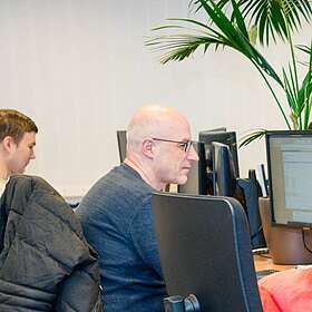 Mitarbeiter sitzen an Ihrem Arbeitsplatz. Ein QFox sitzt auf einem Stuhl.