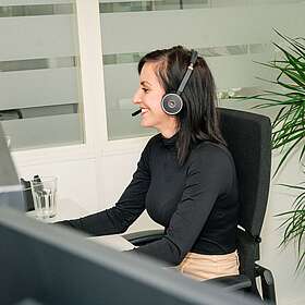 Mitarbeiterin sitzt am Arbeitsplatz und spricht über Headset.