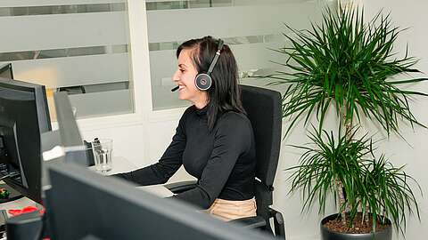 Mitarbeiterin sitzt am Arbeitsplatz und spricht über Headset.
