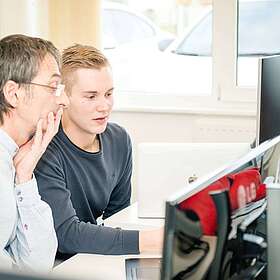 Zwei Mitarbeiter schauen auf einen Monitor.