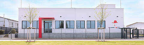 Ein weißes Geschäftsgebäude mit einem roten Eingangsbereich, an dessen Außenwand das Firmenlogo von Leitwerk zu sehen ist.