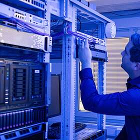 Ein Mann steht im Serverraum. Er überprüft die Kabel. 